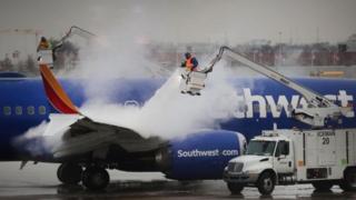 Workers remove ice from an aeroplane in Chicago, which is expected to be one of the worst affected cities