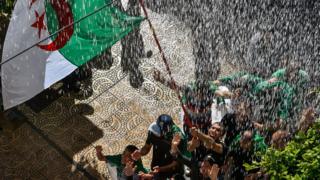 Protesters wave the Algerian flag beneath a shower of water - Friday 10 May